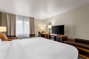 A hotel room with a large bed, a desk with a flat-screen TV, a chair, a sofa, and a window with curtains.