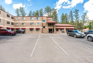 A multi-story hotel with a parking lot, featuring a central entrance and multiple windows.