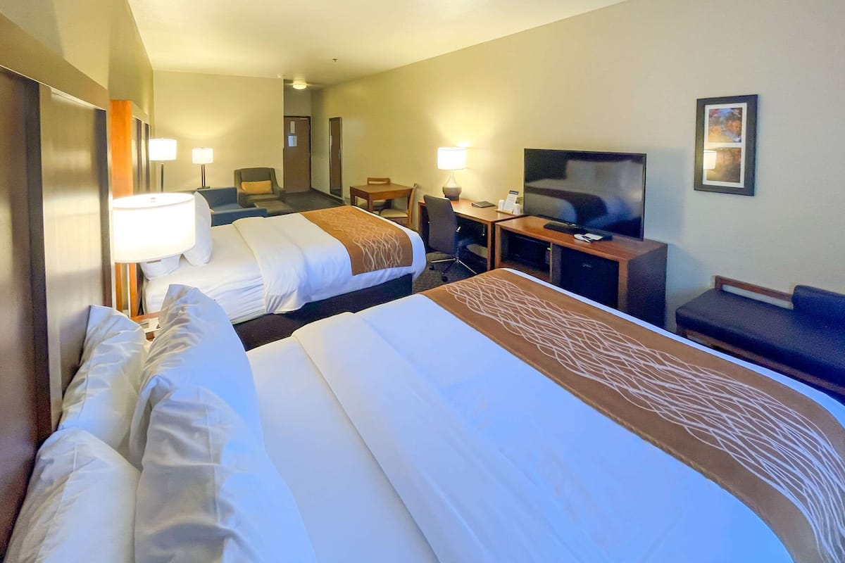 A hotel room with two beds, a desk with a TV, a chair, and a lamp.