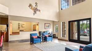 A spacious lobby with a reception desk, two blue armchairs, a large mirror, and a decorative horse sculpture.