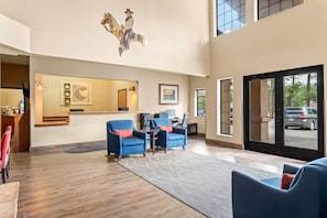 A spacious lobby with a reception desk, two blue armchairs, a large mirror, and a decorative horse sculpture.