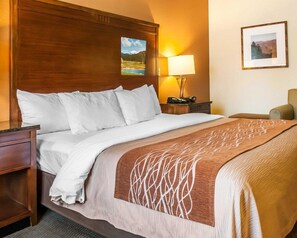 A hotel room with a large bed, a wooden headboard, a nightstand with a lamp, and a framed picture on the wall. - Comfort Inn & Suites Midtown (Ruidoso)