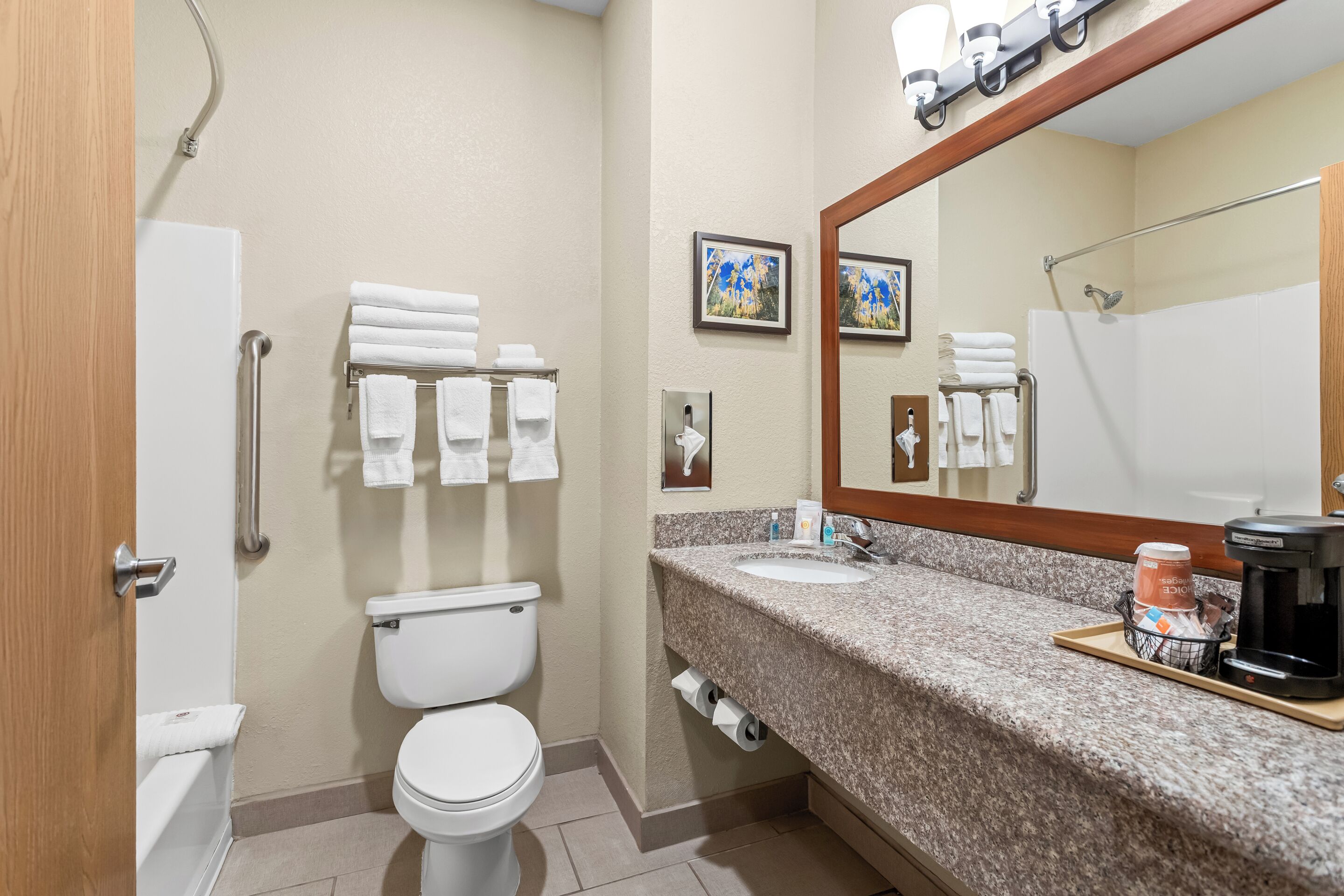 Une salle de bain d’hôtel avec des toilettes, un lavabo et une douche. On y trouve des serviettes et des articles de toilette sur le comptoir.