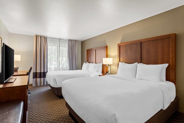 A hotel room with two beds, a desk, a TV, and a window with curtains.