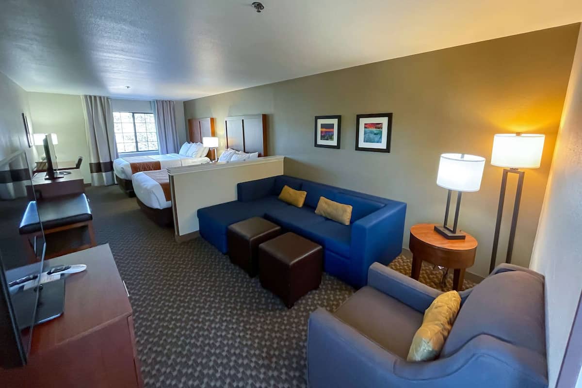 A hotel room with a bed, a blue sofa, a desk with a computer, and two bedside lamps.