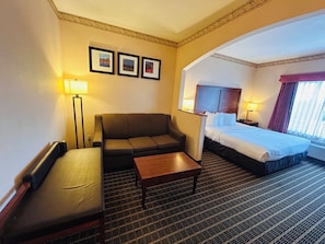 A hotel room with a sofa, a bed, a small table, and a carpeted floor. - Sylvania Inn & Suites Tigard Portland I-5 (Portland)