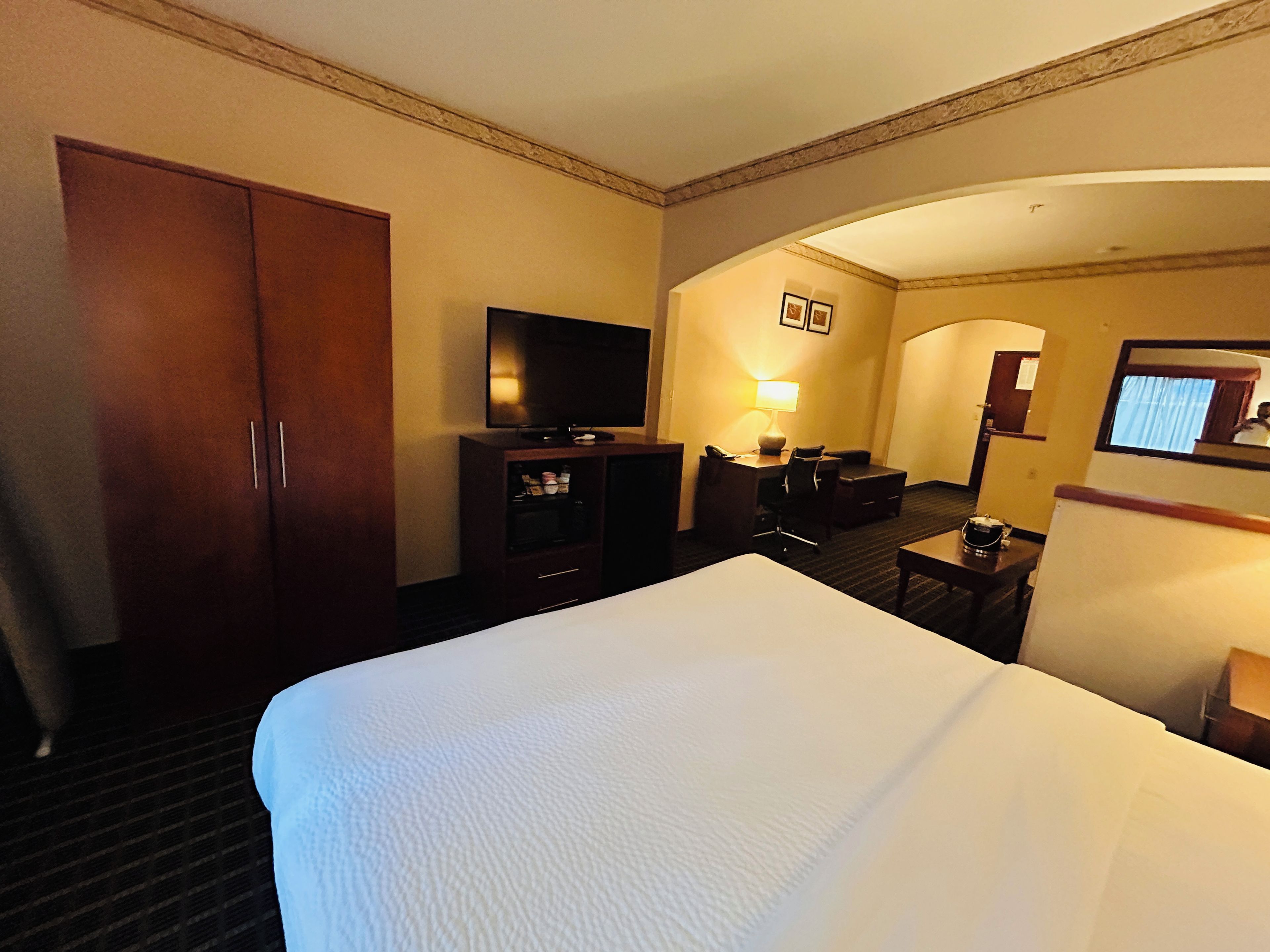 A hotel room with a large bed, a television, a desk with a chair, and a wardrobe.