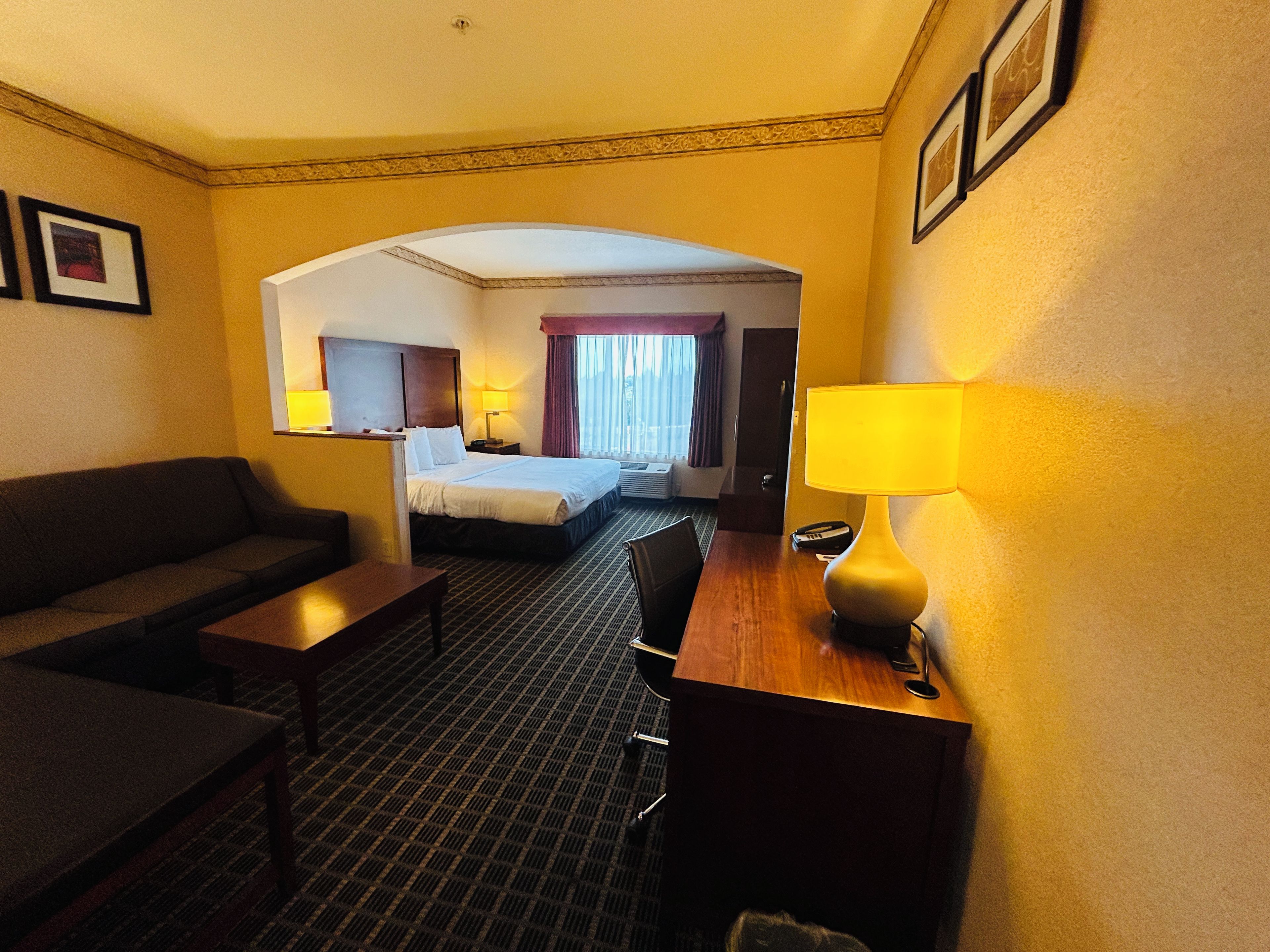 A hotel room with a bed, a desk, a chair, a sofa, and a lamp.