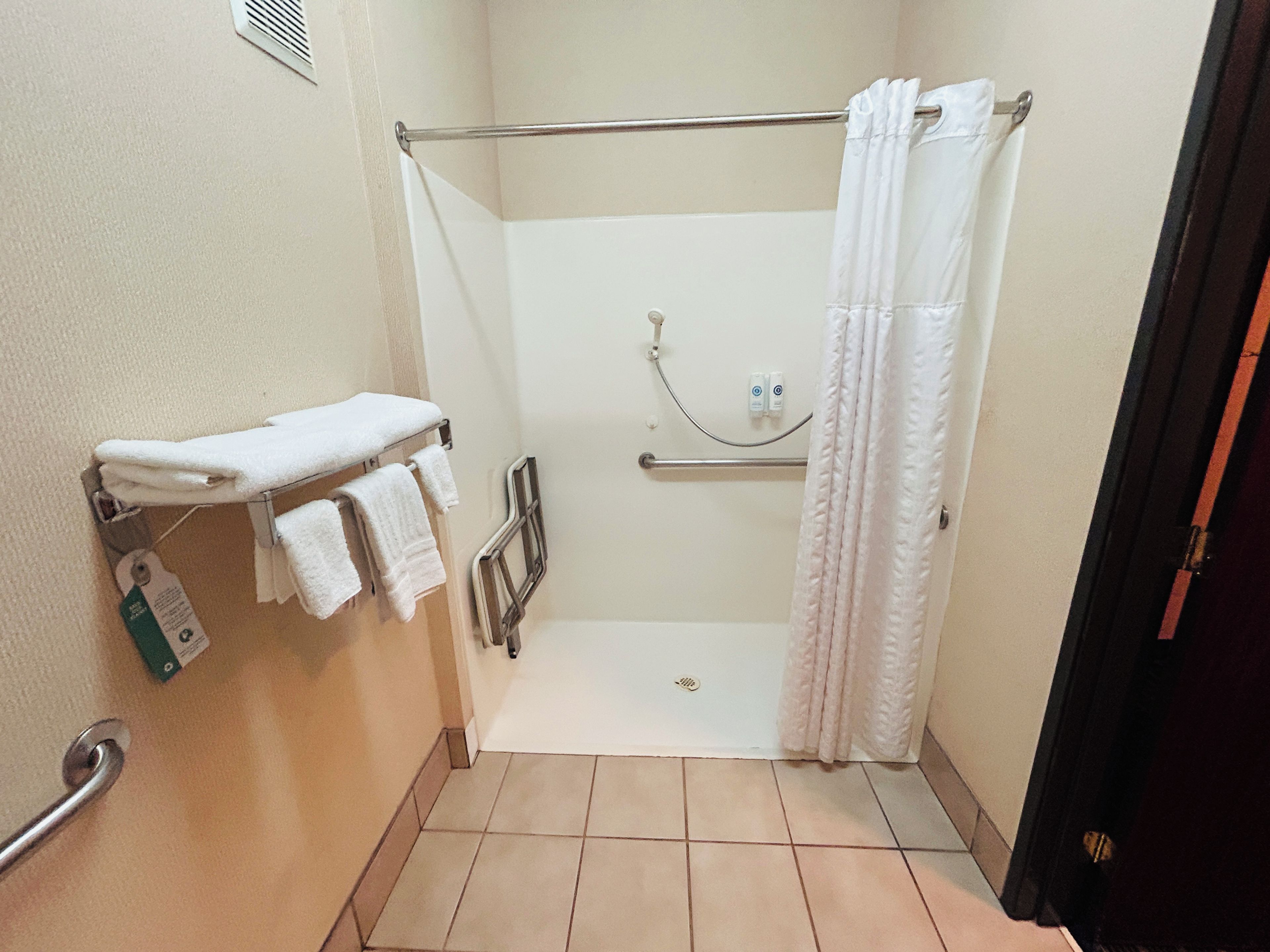 A small, enclosed shower area with a grab bar, a towel rack with folded towels, and a shower curtain.
