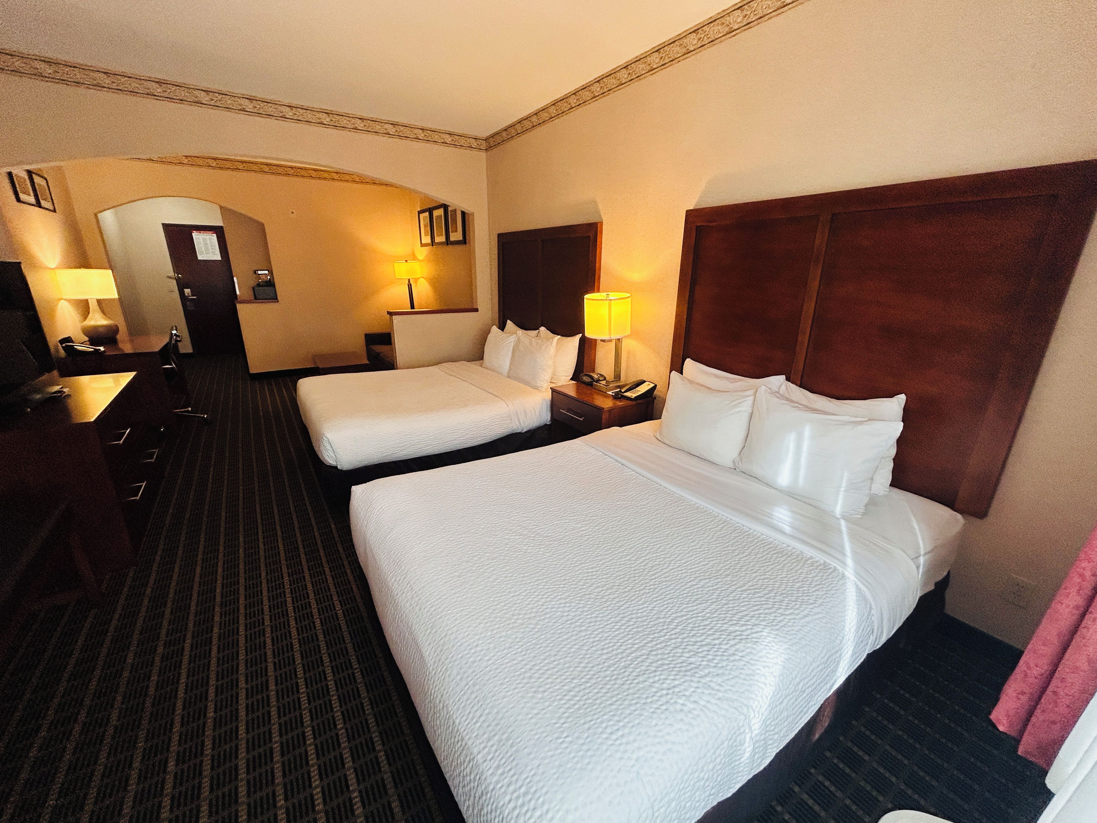 Ein Hotelzimmer mit zwei Betten, einem Schreibtisch, einem Stuhl und einer Lampe.