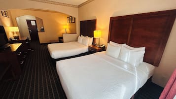 Ein Hotelzimmer mit zwei Betten, einem Schreibtisch, einem Stuhl und einer Lampe.