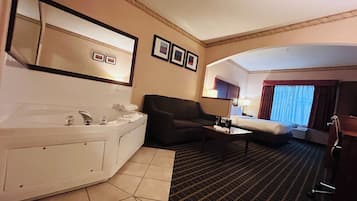 Una habitación de hotel con una bañera grande, un sofá, una mesa de centro y una cama.