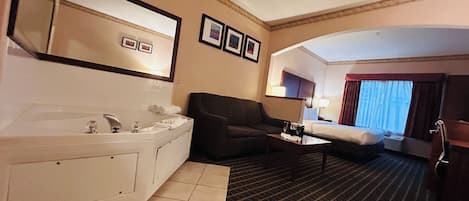 A hotel room with a large bathtub, a sofa, a coffee table, and a bed.