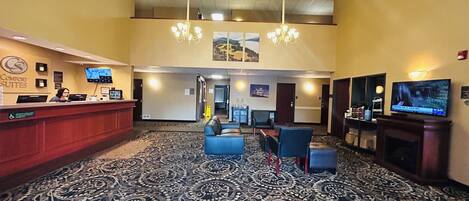 Un hall de hotel con una recepción, zona de estar y una pantalla de televisión.