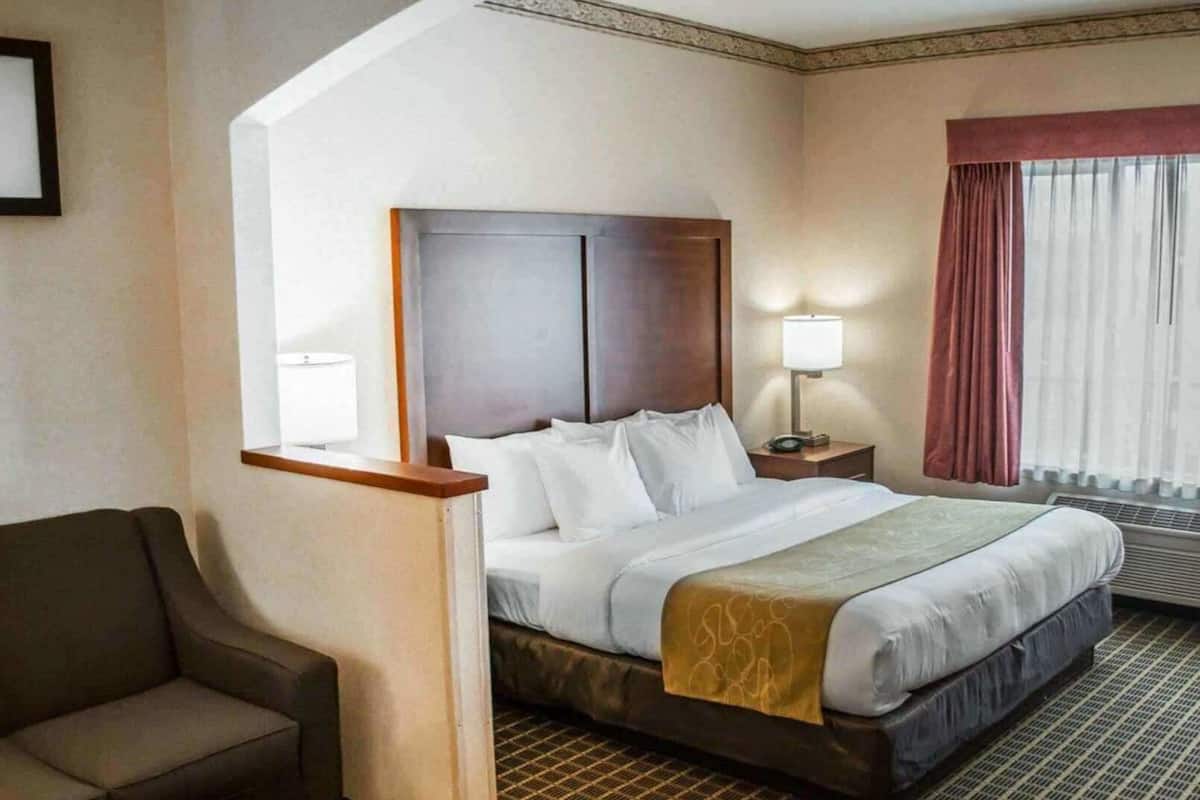 Una camera d'albergo con un letto, una scrivania, una sedia, una lampada e una finestra con tende.