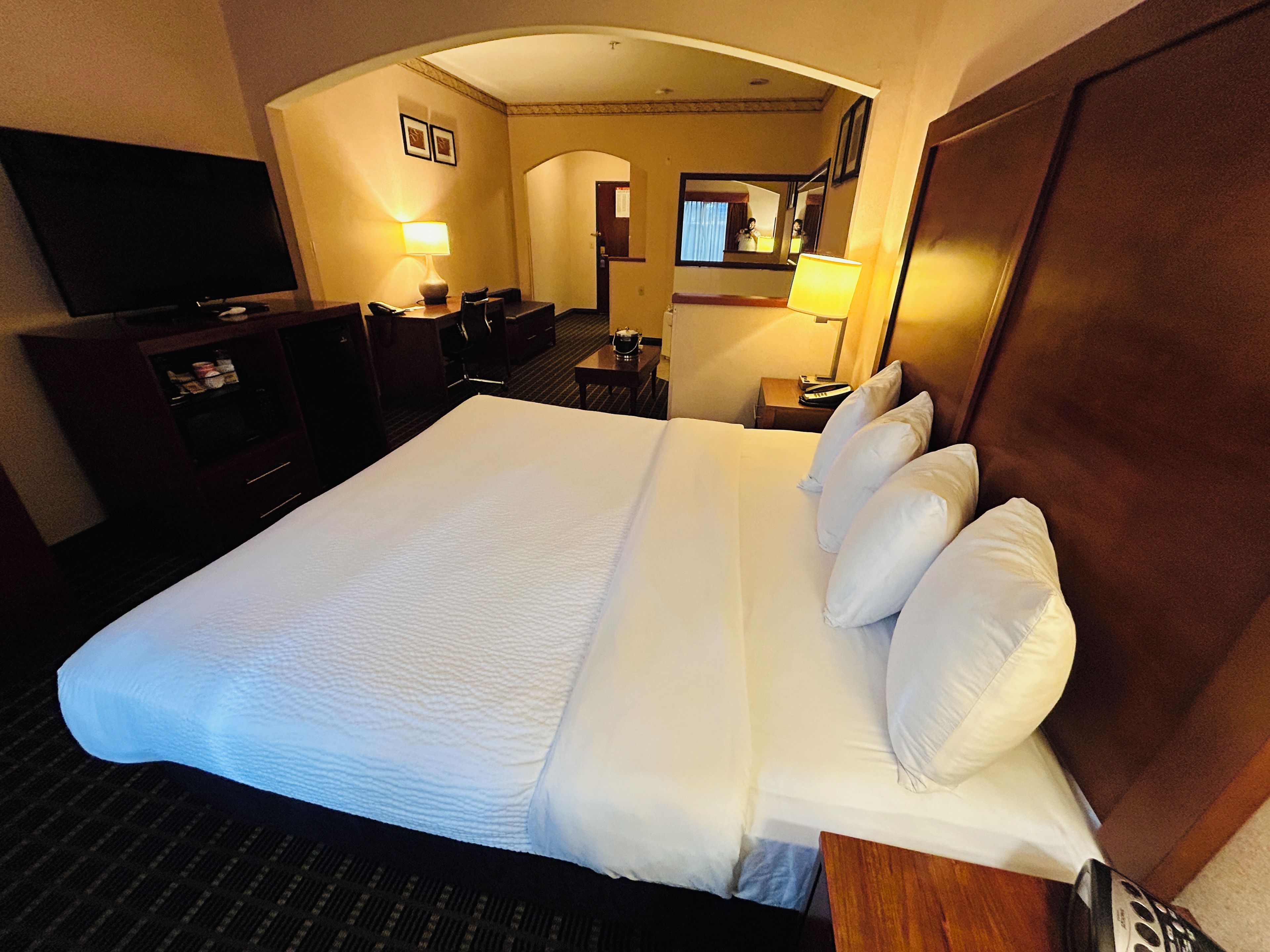 A hotel room with a large bed, a desk, a chair, a television, and a mirror.