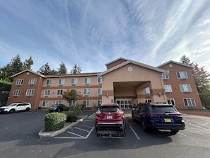 A multi-story hotel with a central entrance, parking lot, and surrounding trees. - Sylvania Inn & Suites Tigard Portland I-5 (Portland)