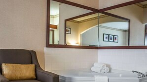 A bathroom with a large mirror, a bathtub, a chair, and a towel. - Comfort Suites Portland Southwest (Portland)