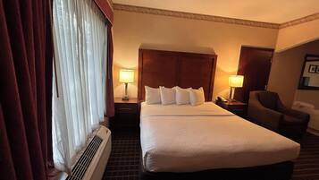 A hotel room with a large bed, two bedside lamps, a chair, and a window with curtains.