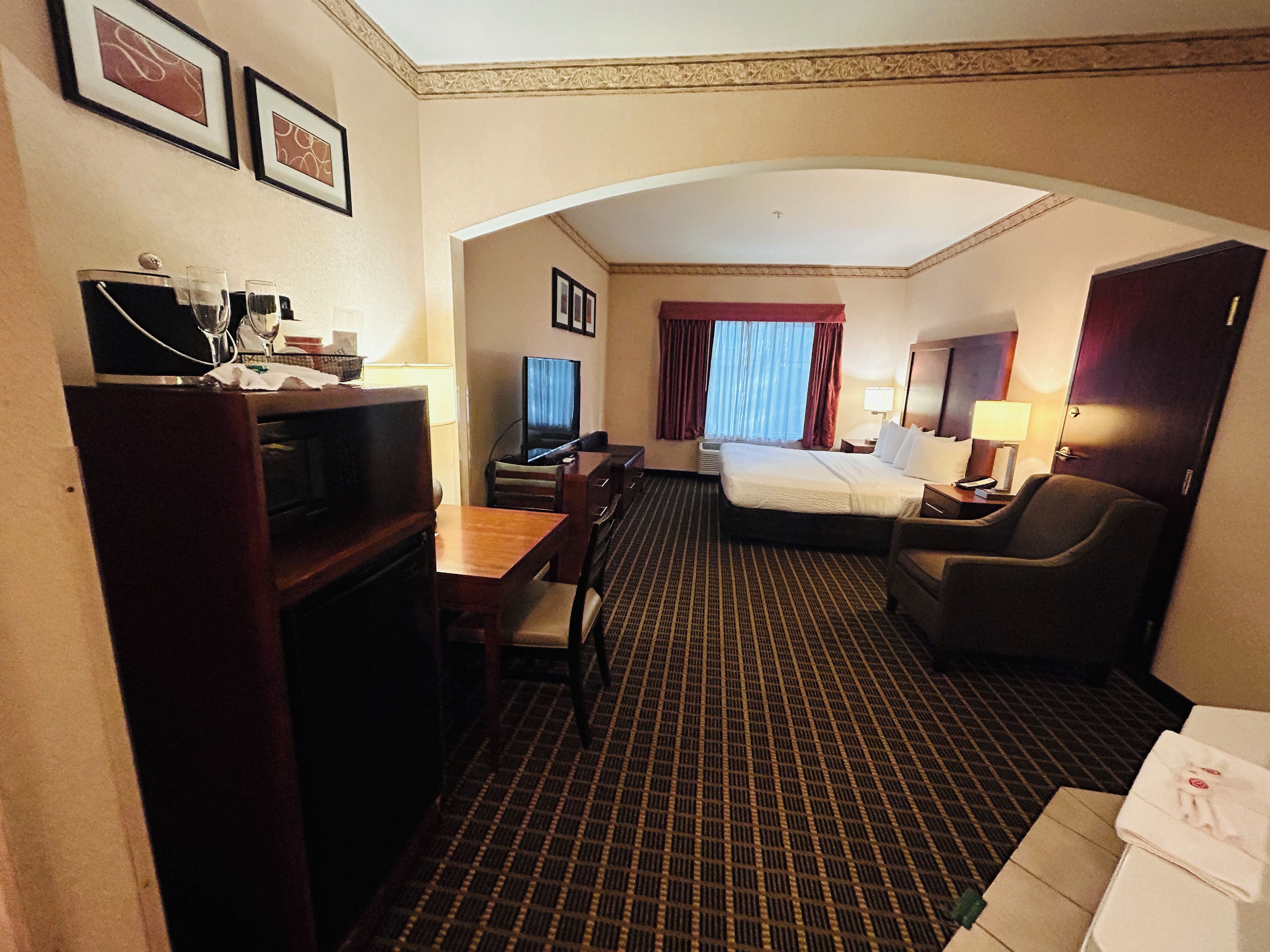 A hotel room with a bed, desk, chair, television, and a small table with a lamp.