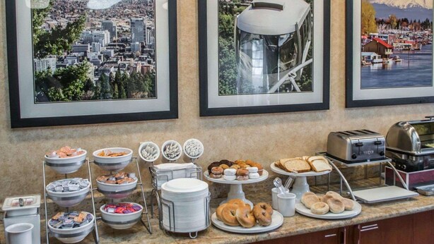 A breakfast buffet with various food items and a coffee station, set against a backdrop of framed cityscape photographs. - Comfort Suites Portland Southwest (Portland)