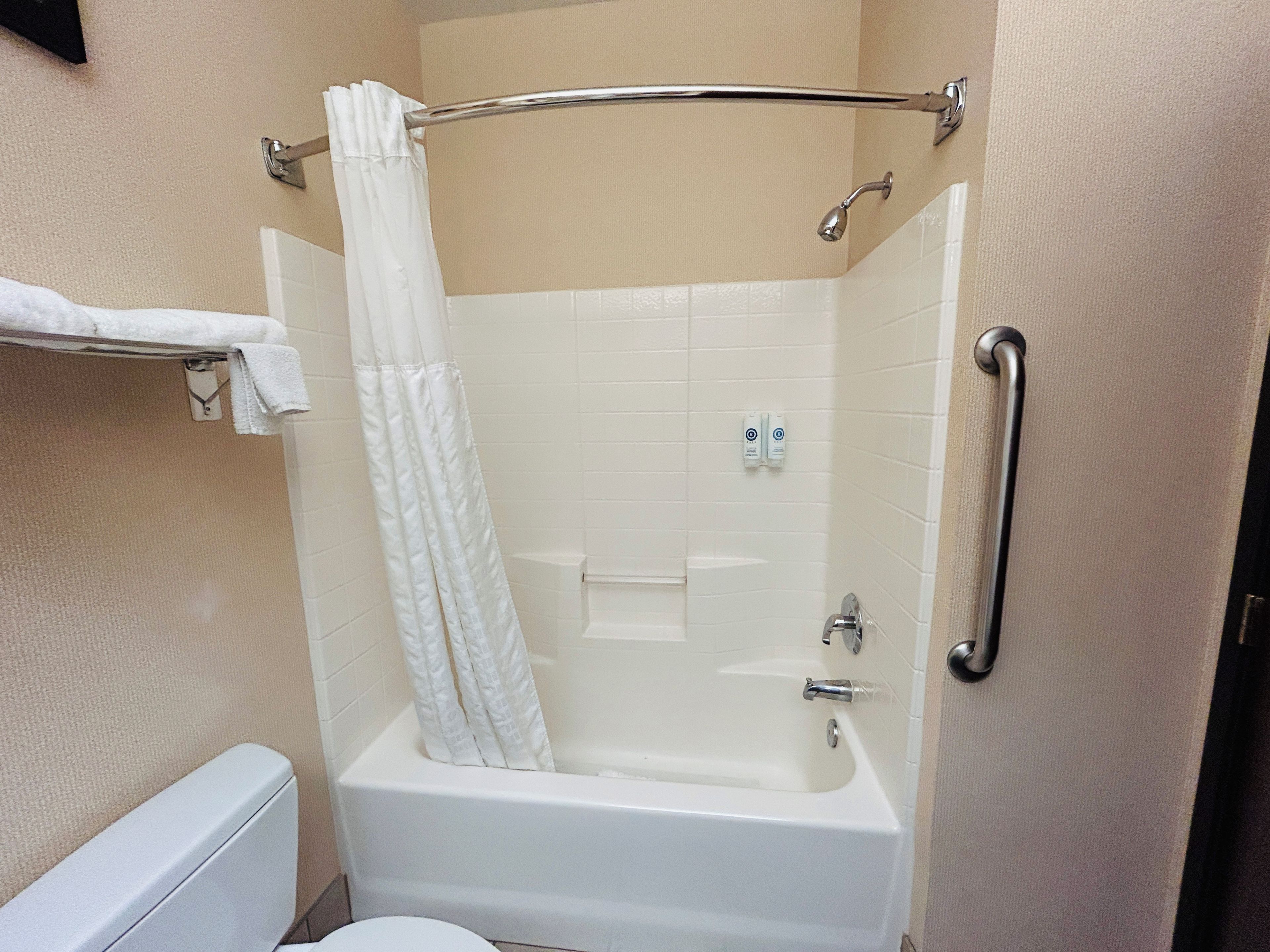 A bathroom with a bathtub, a shower curtain, a towel rack, and a handrail.
