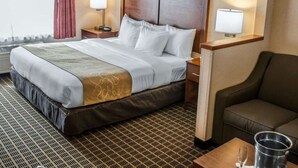 A hotel room with a bed, bedside lamps, a nightstand, a sofa, and a small table with a glass and a metal container. - Comfort Suites Portland Southwest (Portland)