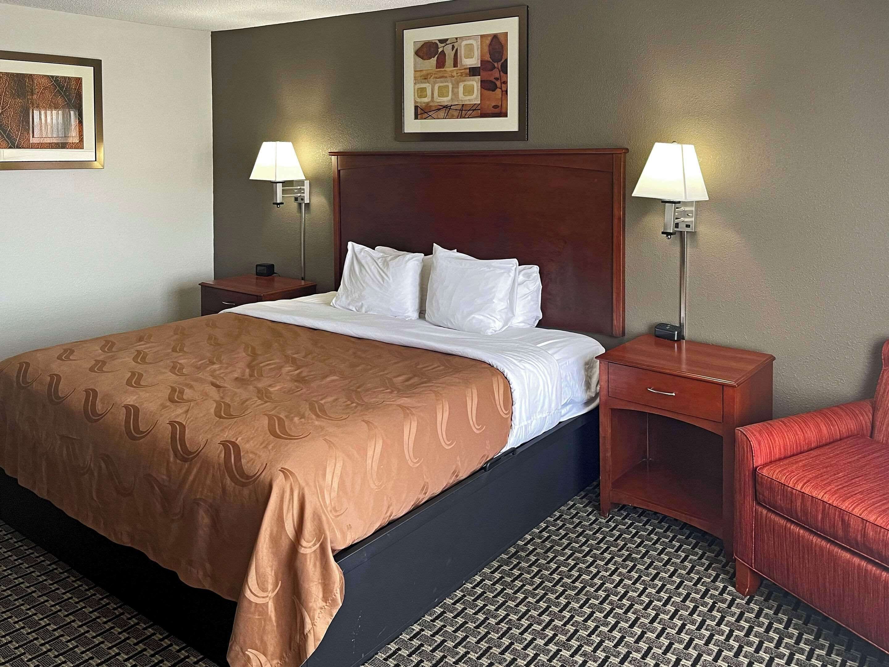 A hotel room with a large bed, two bedside tables, a red armchair, and two wall-mounted lamps.