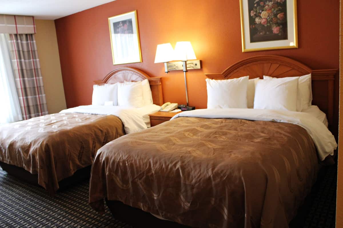 A hotel room with two beds, a nightstand with a lamp, and a painting on the wall.