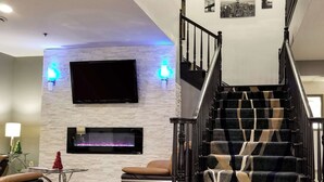 A modern living room with a fireplace, a staircase, and a flat-screen TV mounted on the wall. - Quality Inn & Suites Cincinnati Sharonville (Sharonville)
