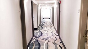 A hotel hallway with a patterned carpet, doors on both sides, and a sign at the end. - Quality Inn & Suites Cincinnati Sharonville (Sharonville)
