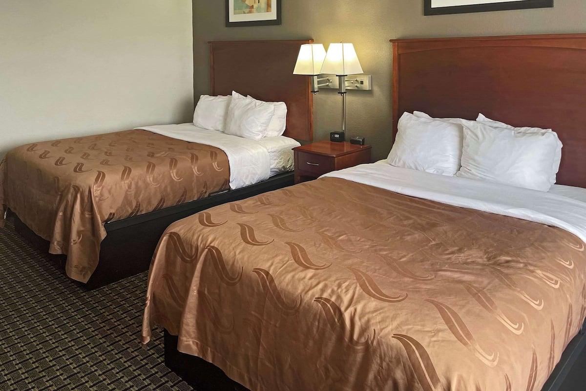 Two single beds with brown headboards and white bedding, a nightstand with a lamp, and a clock.