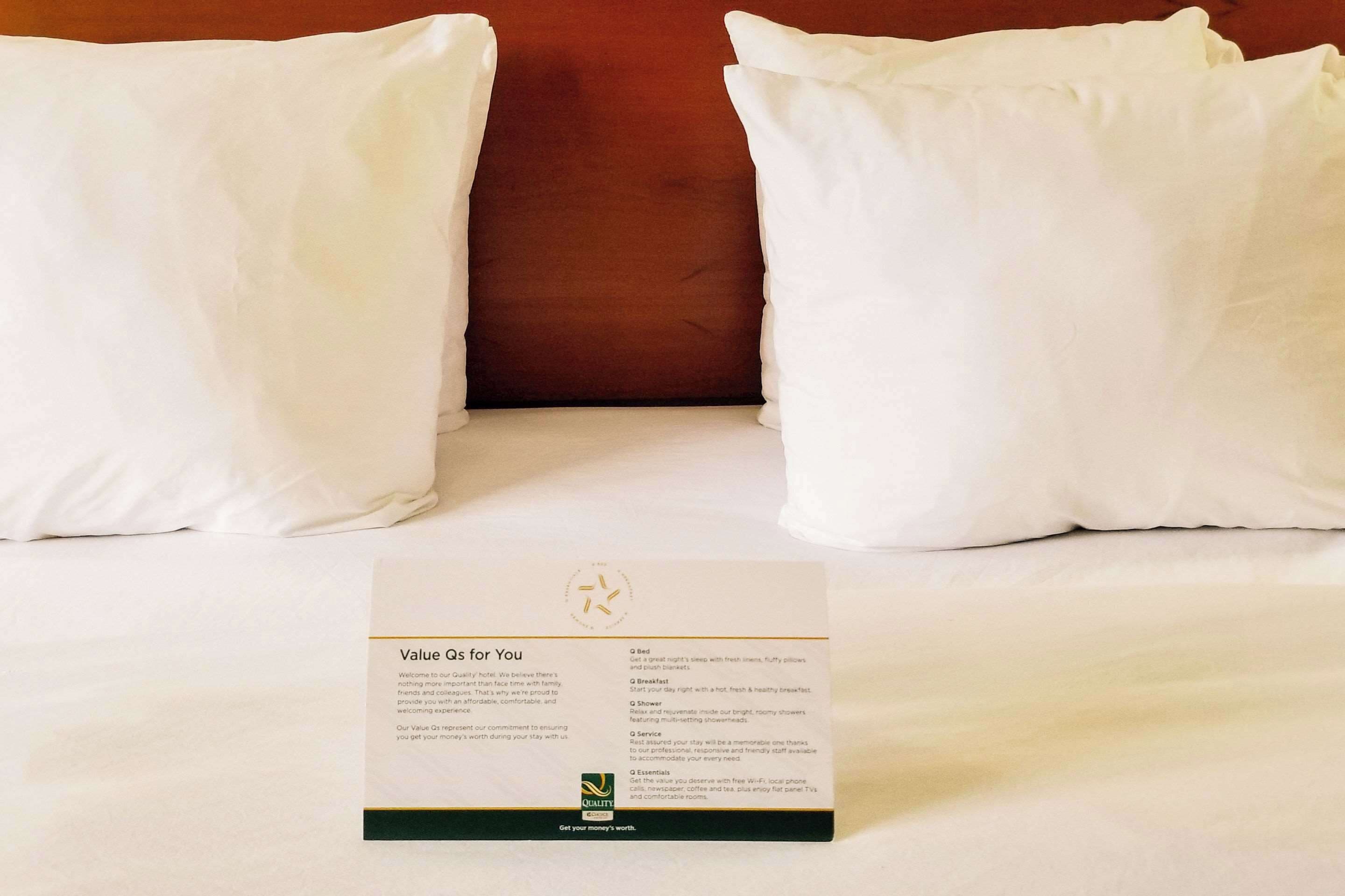Un llit d'hotel amb almoades blanques i una tarjeta de benvinguda que detalla els serveis.