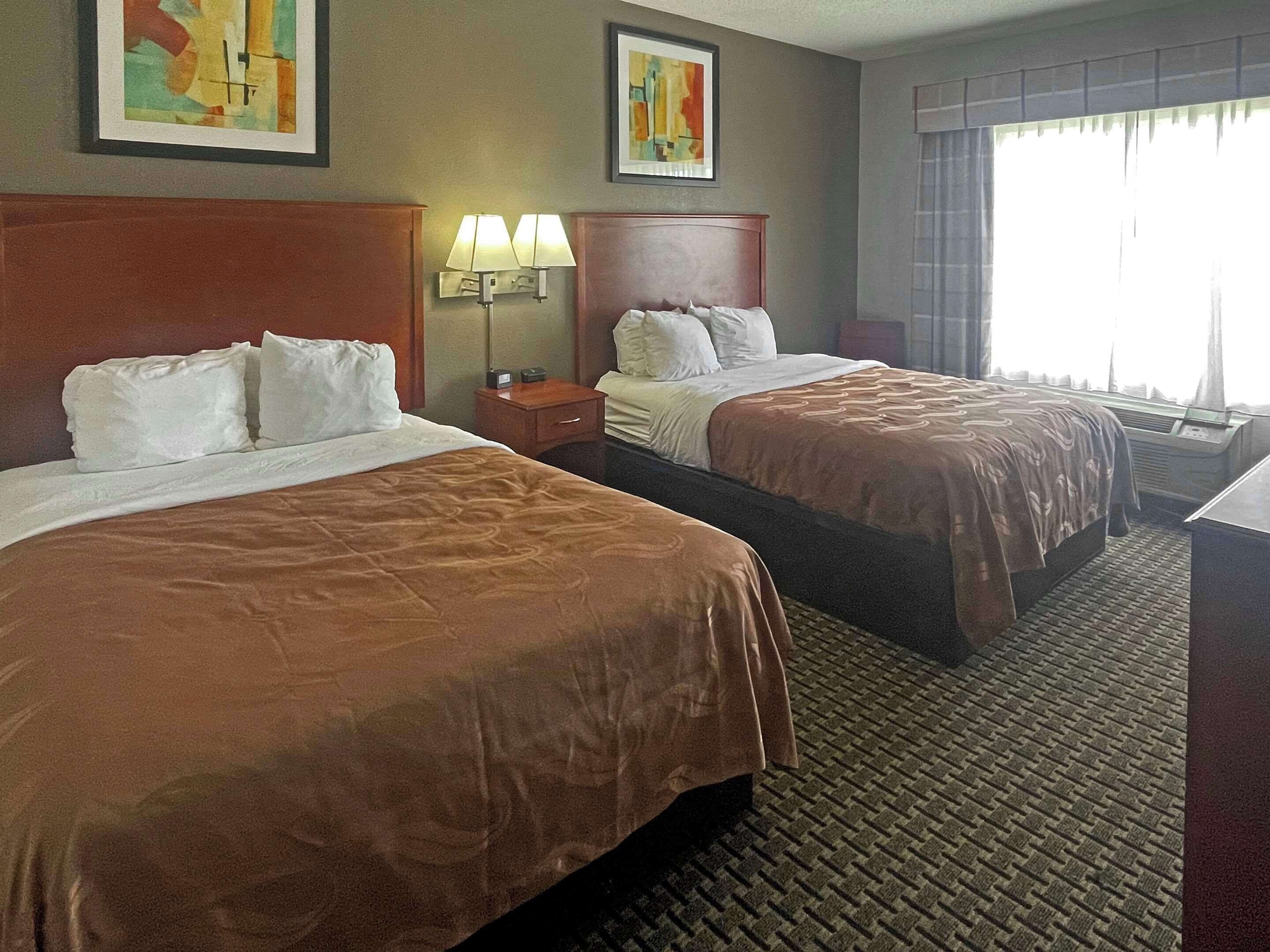 A hotel room with two beds, a nightstand, a lamp, and artwork on the walls.