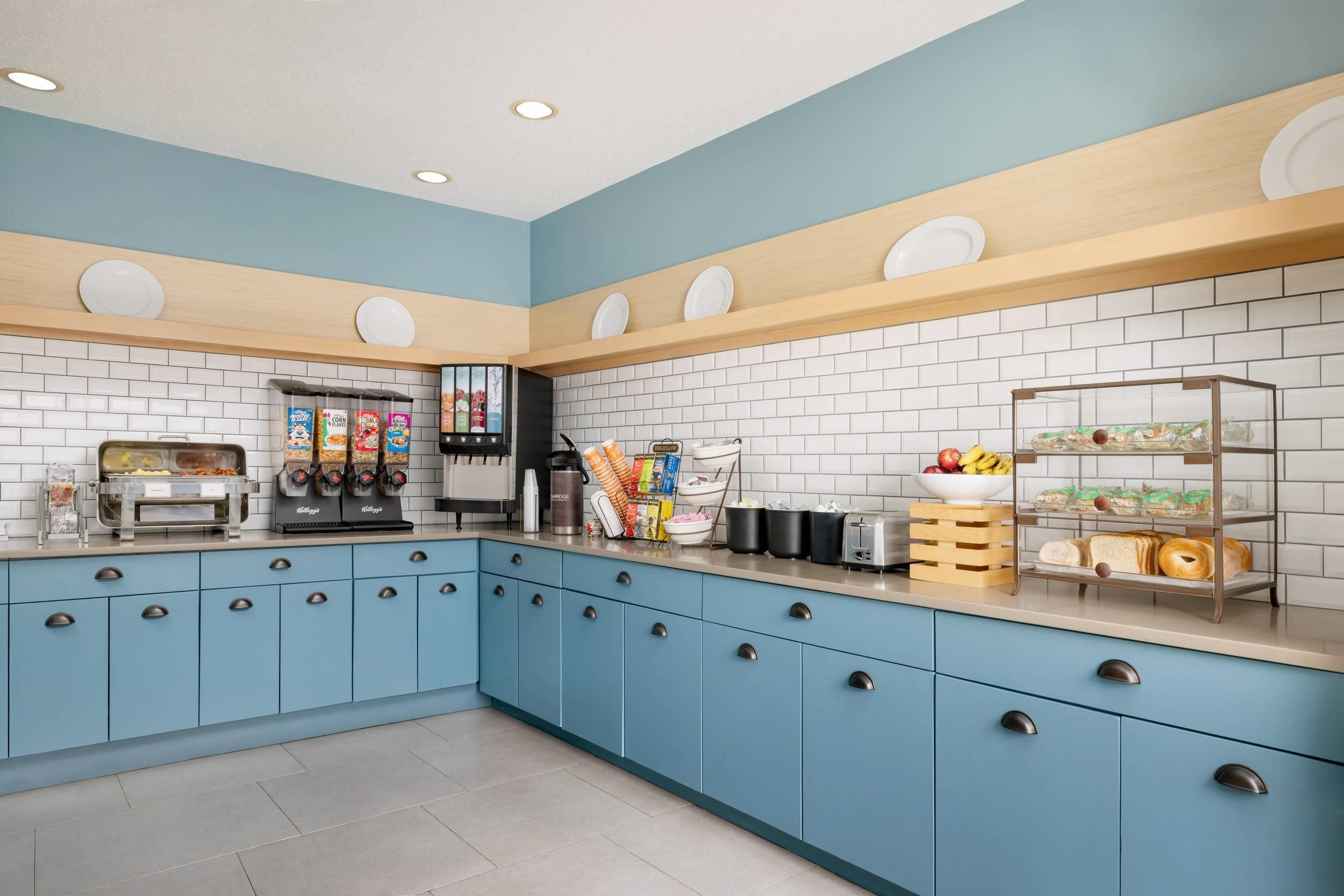 A kitchen with blue cabinets, white tiled backsplash, and various food items and appliances.