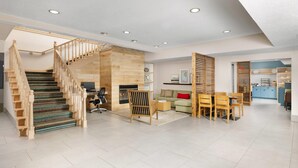A spacious living area with a wooden staircase, a fireplace, a dining area, and a kitchen visible through an open door. - Country Inn & Suites by Radisson, Springfield, OH (Springfield)