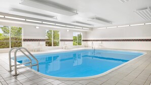 A swimming pool with a metal ladder, white tiled floor, and a view of greenery outside. - Country Inn & Suites by Radisson, Springfield, OH (Springfield)