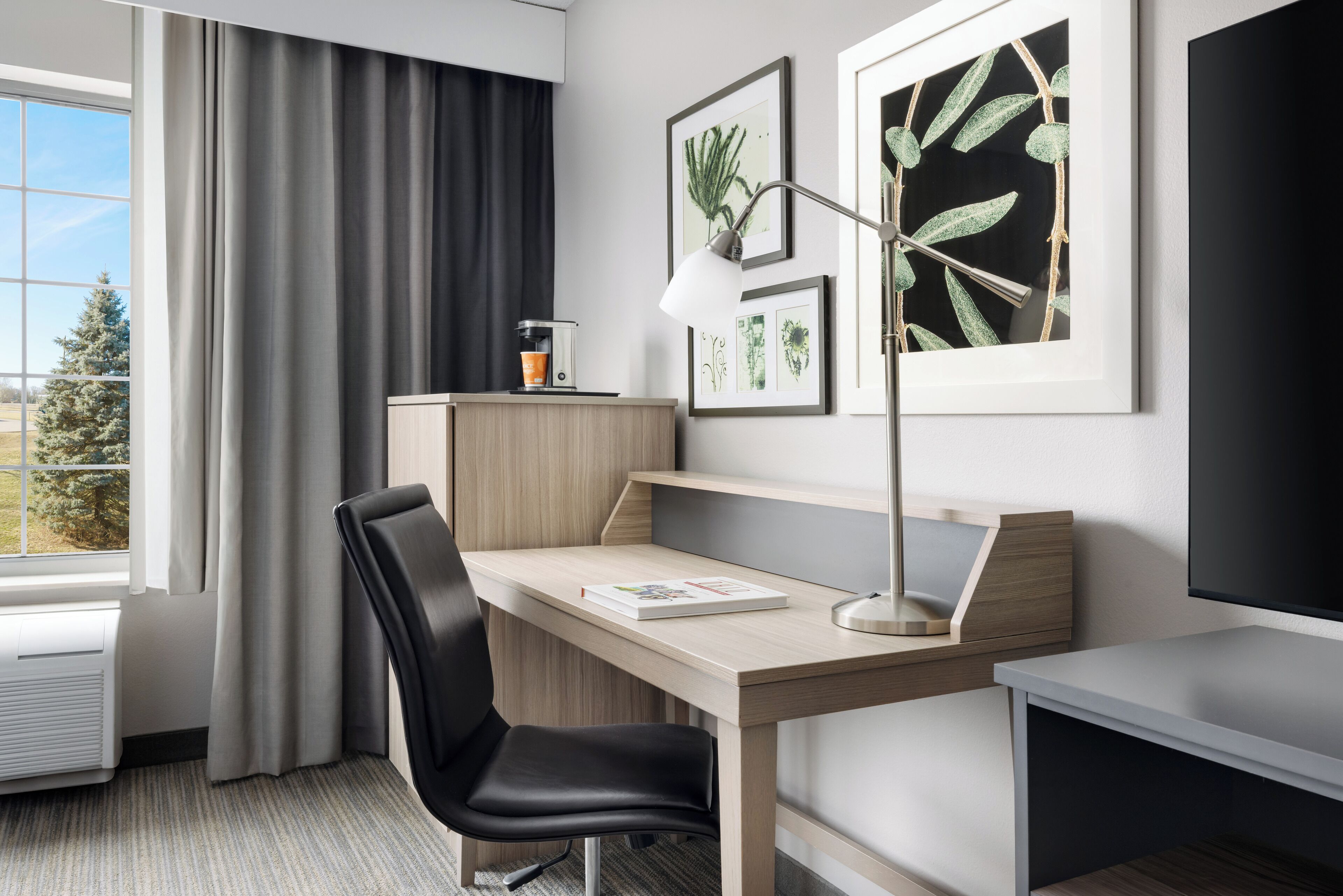 A modern hotel room with a desk, chair, and a large window with curtains.