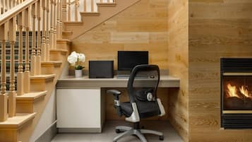 Una oficina moderna en casa con una escalera de madera, un escritorio con una computadora portátil, una silla de oficina negra y una chimenea.