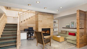 A modern living room with a wooden staircase, a fireplace, a sofa, and a coffee table. - Country Inn & Suites by Radisson, Springfield, OH (Springfield)
