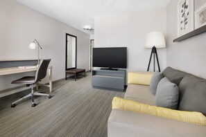 A modern hotel room with a desk, chair, television, sofa, and lamps. - Country Inn & Suites by Radisson, Springfield, OH (Springfield)