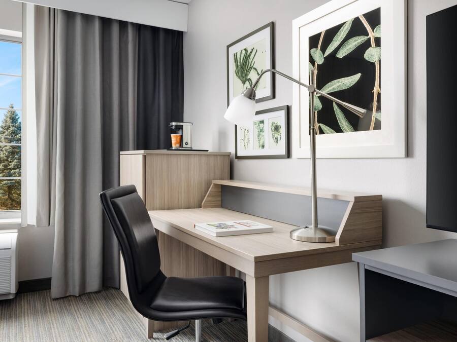 Quarto de hotel moderno com escrivaninha, cadeira e uma grande janela com cortinas.