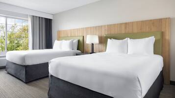 Habitación de hotel con dos camas, un ventanal con cortinas y un cabecero de madera.
