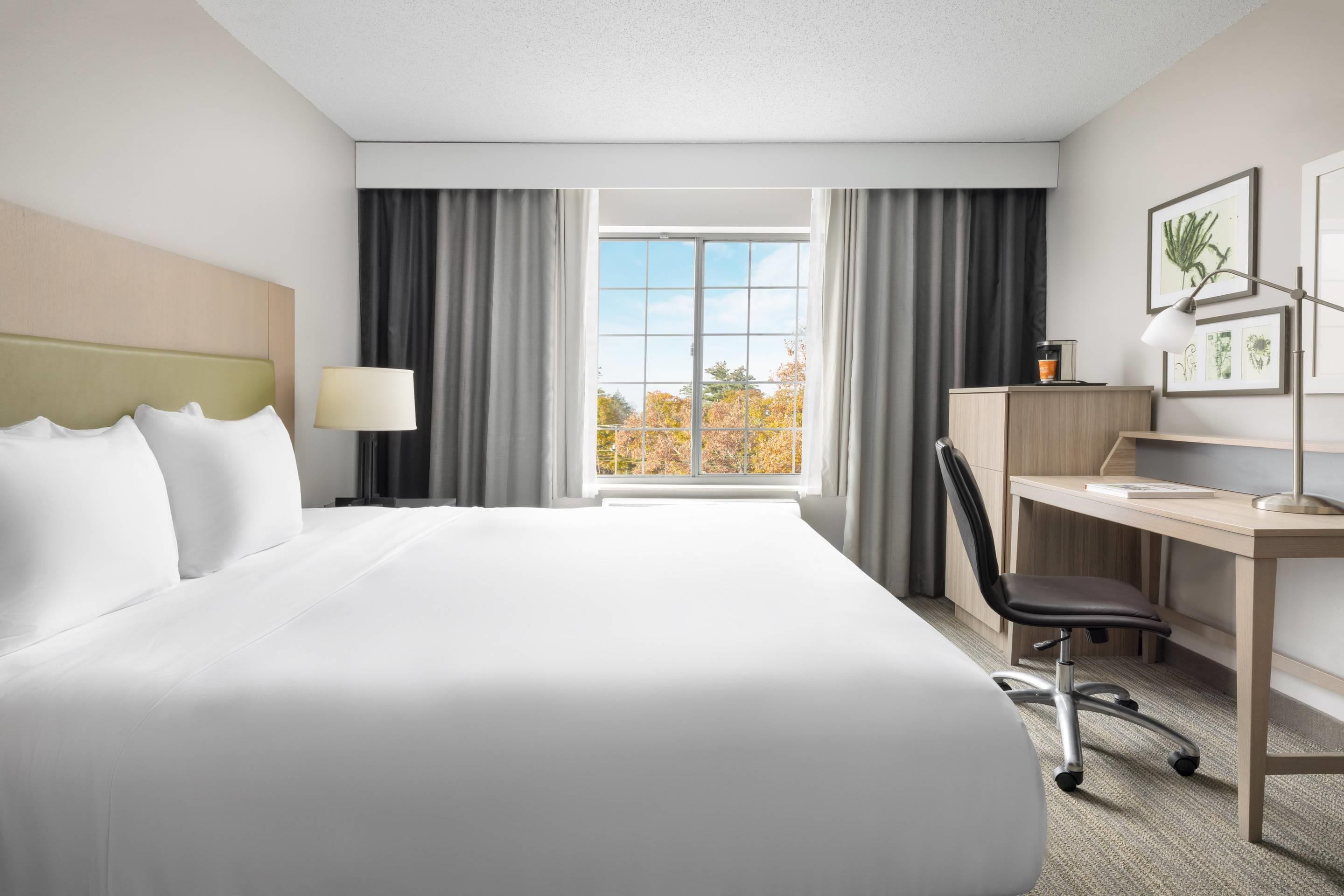 A hotel room with a large bed, a desk, a chair, a lamp, and a window with curtains.