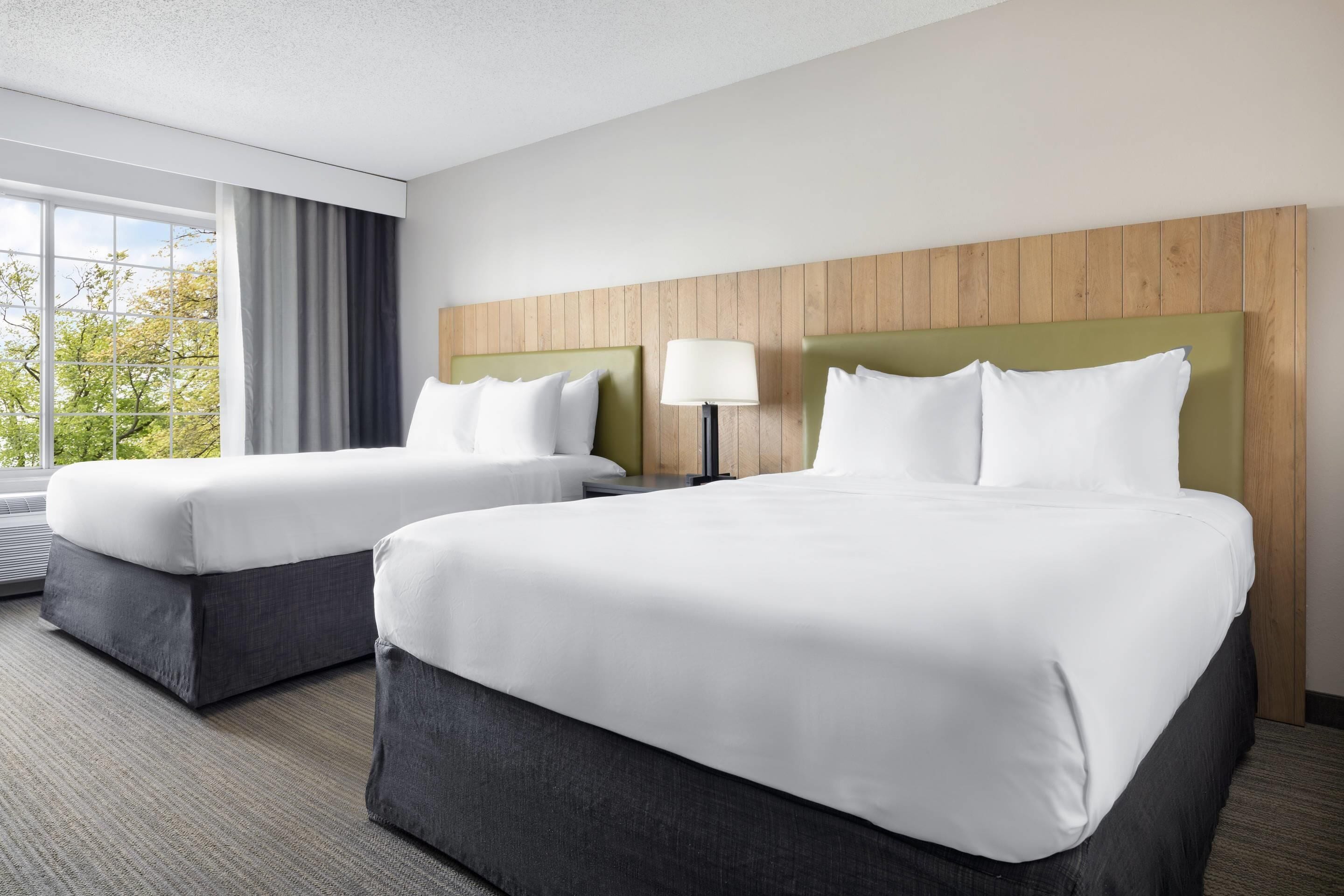 A hotel room with two beds, a large window with curtains, and a wooden headboard.