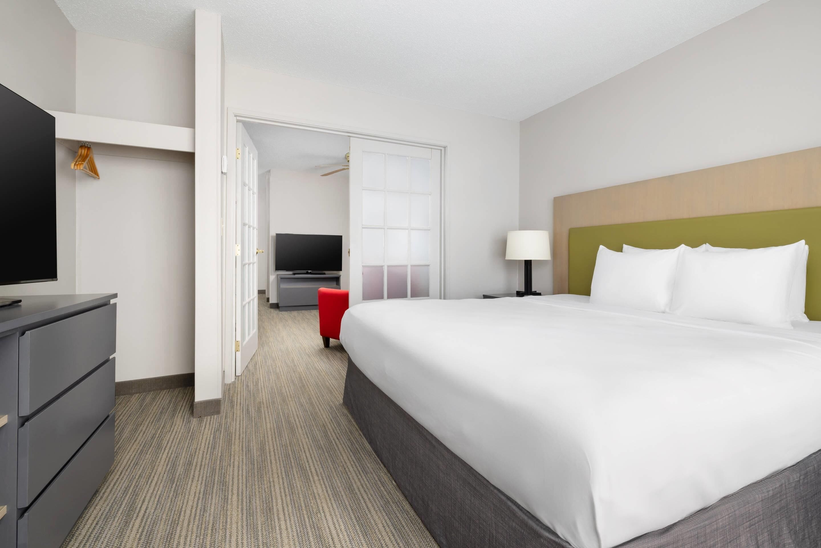 A hotel room with a large bed, a desk with a TV, a lamp, and a red chair.