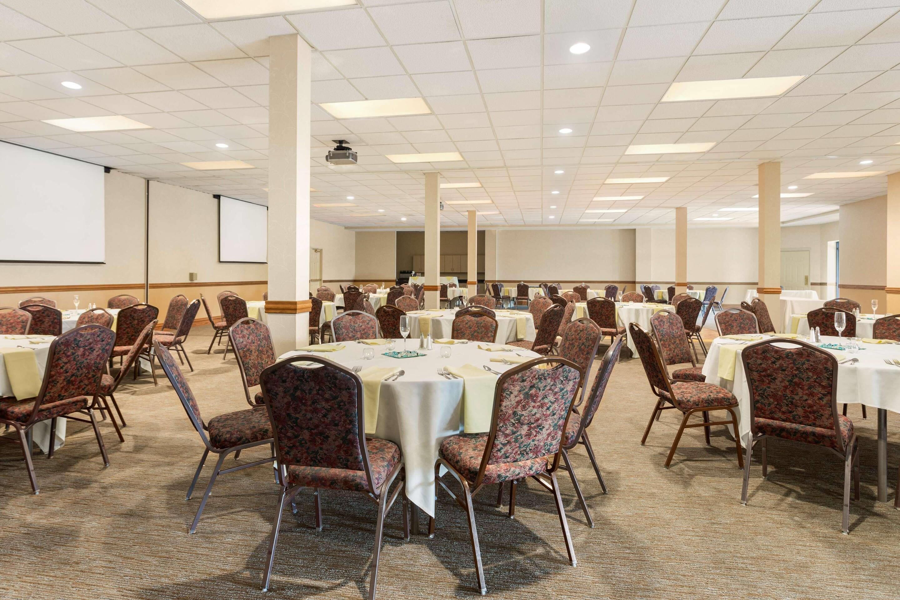 A large conference room with multiple round tables and floral-patterned chairs, equipped with white tablecloths and glassware.