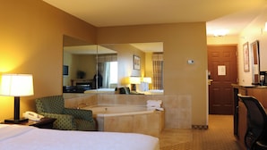 A hotel room with a bed, a chair, a desk, a mirror, a bathtub, and a door.
