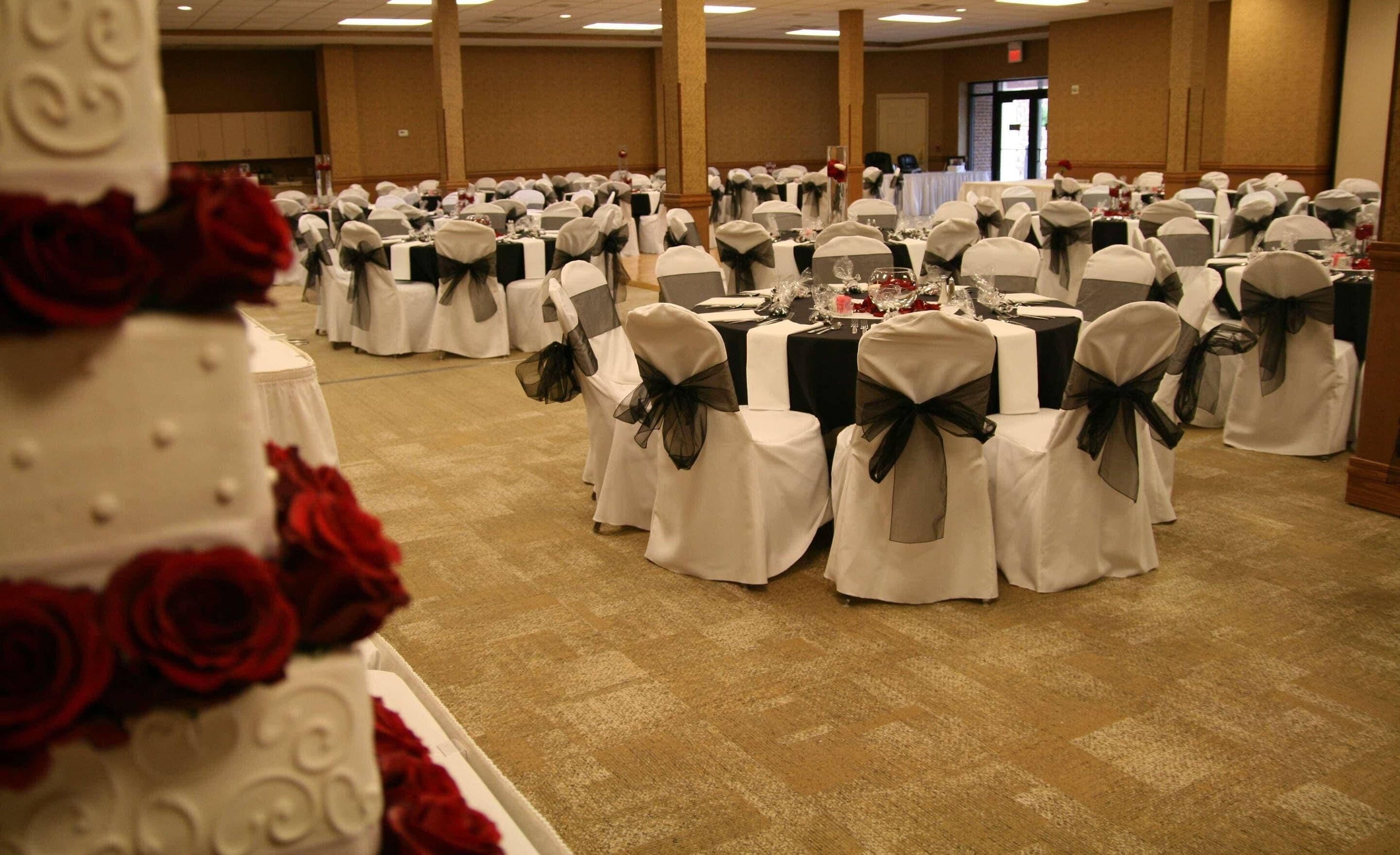A banquet hall with round tables covered in white tablecloths and chairs with black bows.