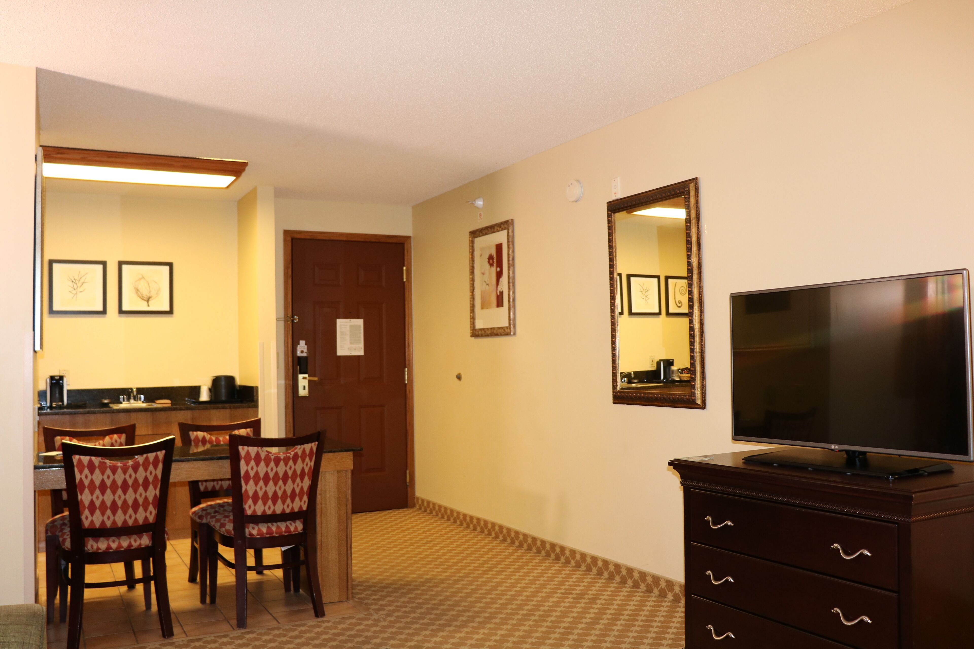 A hotel room with a dining area, a TV, and a mirror.
